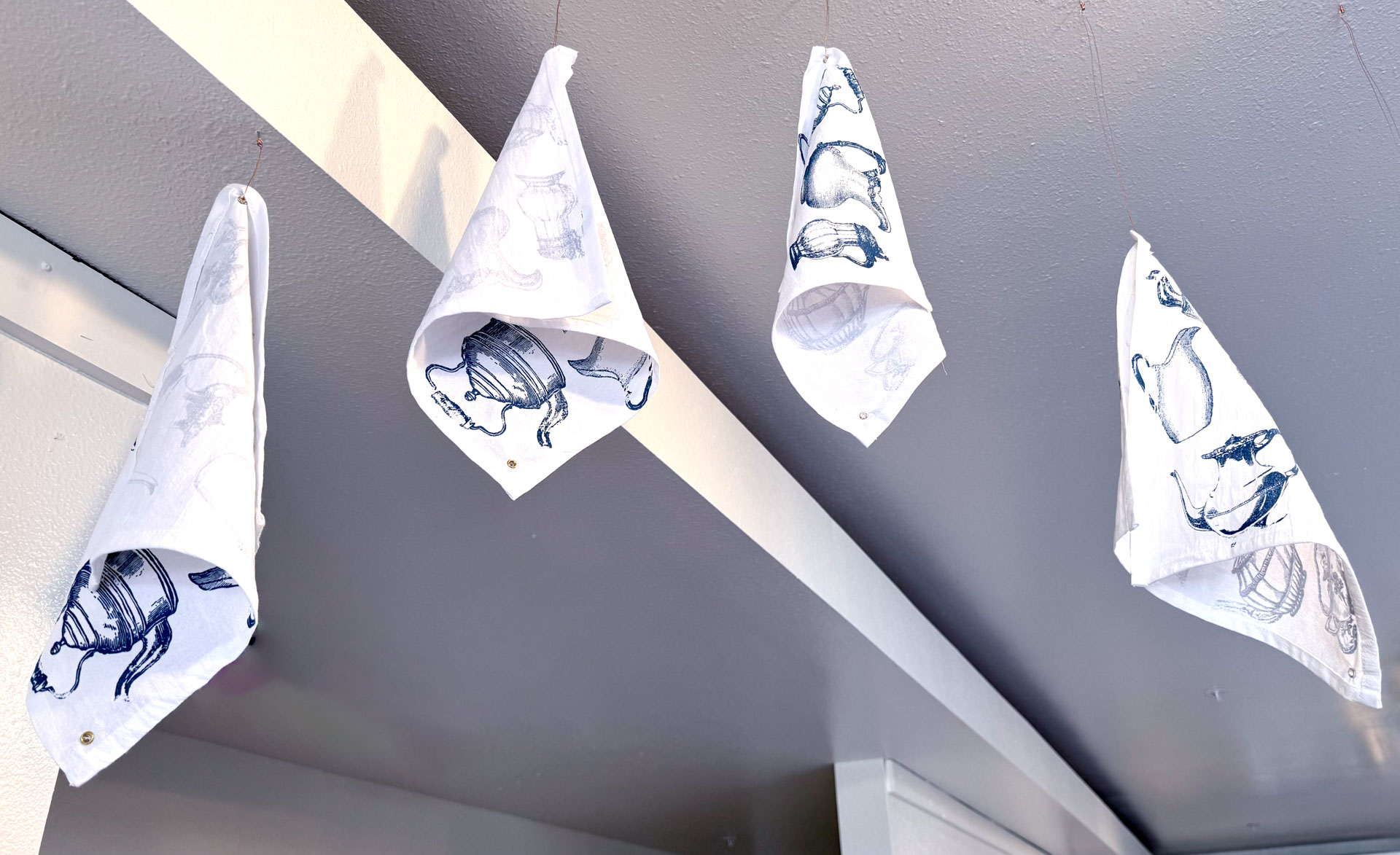 installation with silkscreen napkins attached to ceiling in an arch travelling from a box to a pitcher