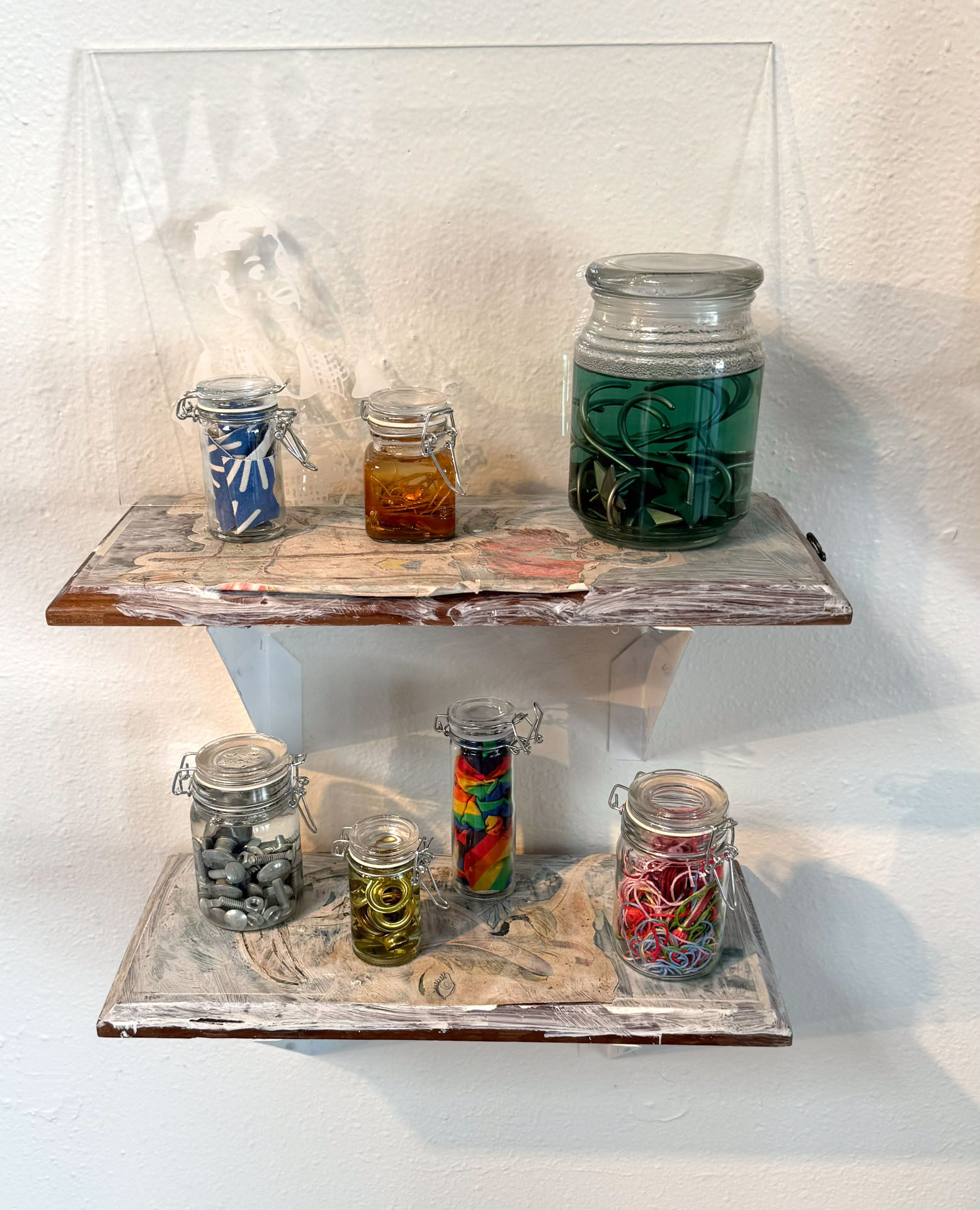 wall installation with glass jars containing harware, cutlery, yarn, fabric, collaged shelves