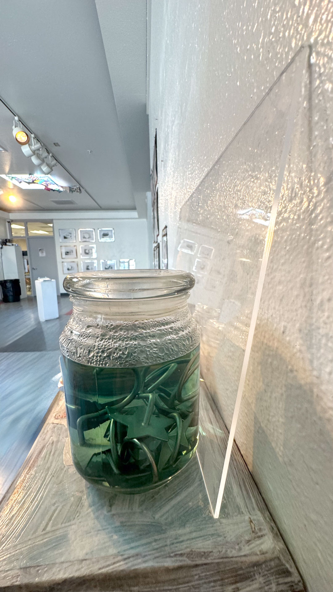 wall installation with glass jars containing harware, cutlery, yarn, fabric, collaged shelves