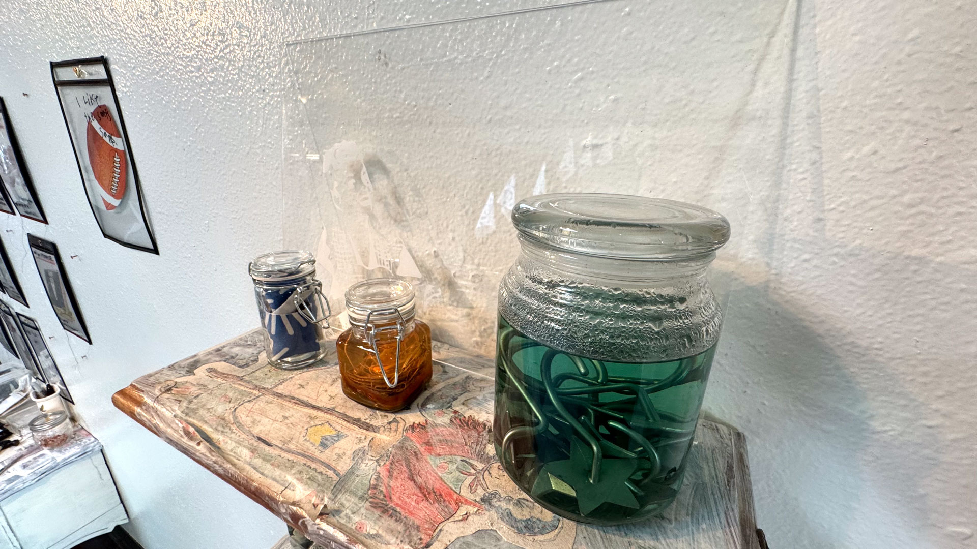 wall installation with glass jars containing harware, cutlery, yarn, fabric, collaged shelves